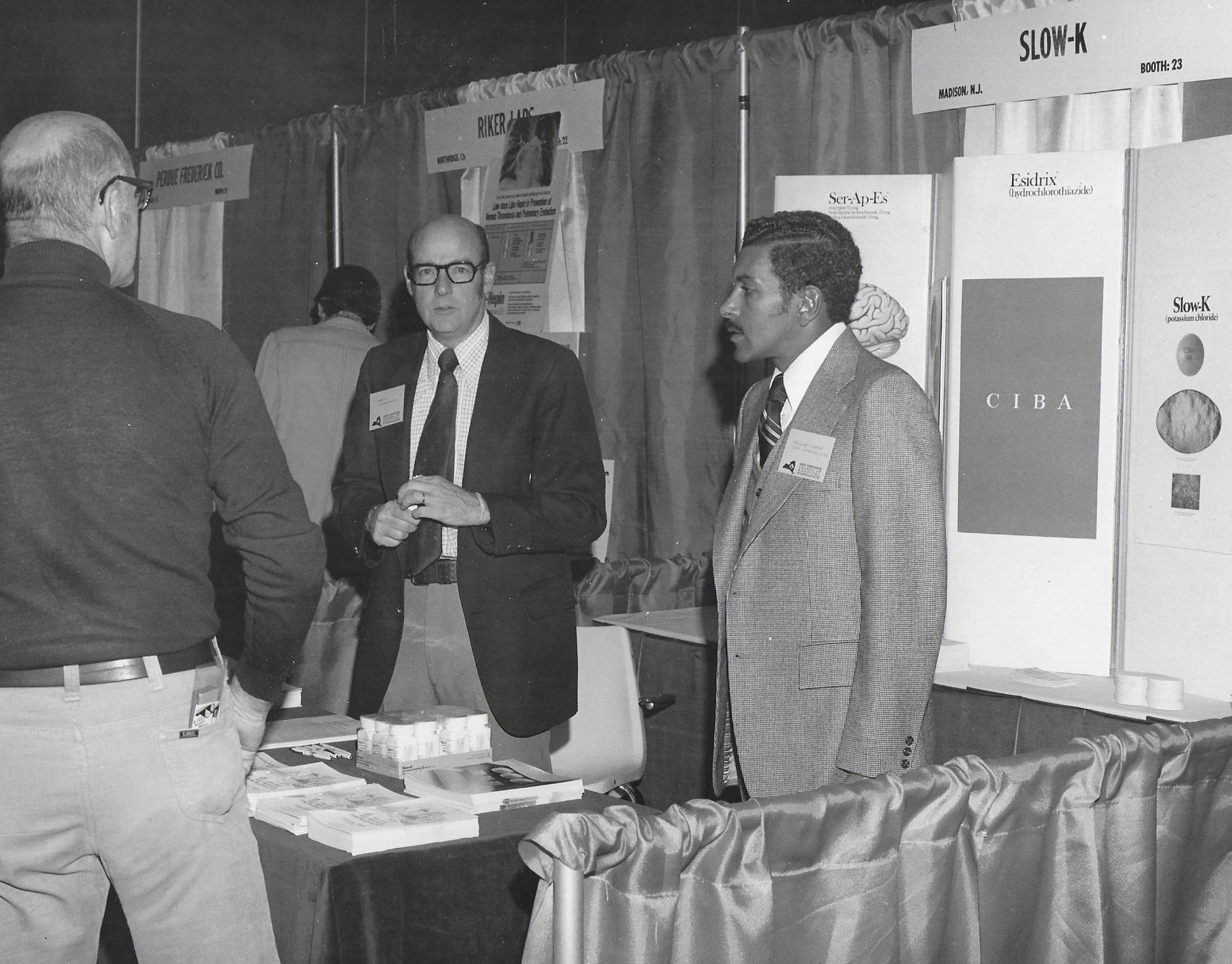 Two Men Standing at Exhibit Booth in 1977